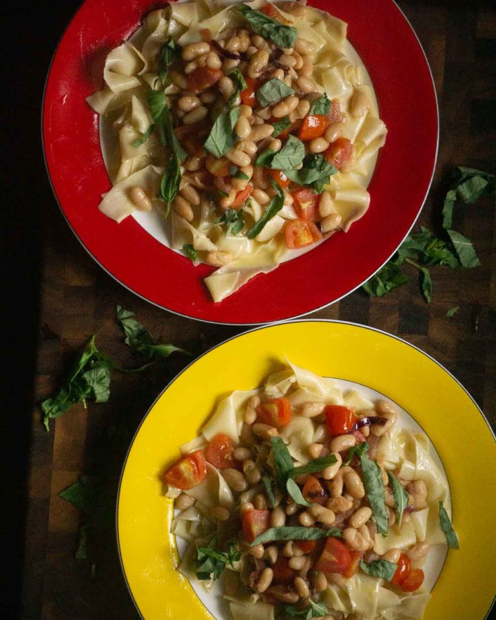 two plates of pasta with white beans, caramelized onions, cherry tomatoes, and basil