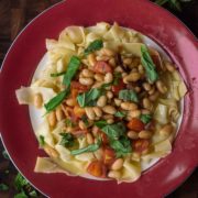 pasta with white beans, caramelized onions, cherry tomatoes, and basil on red plate